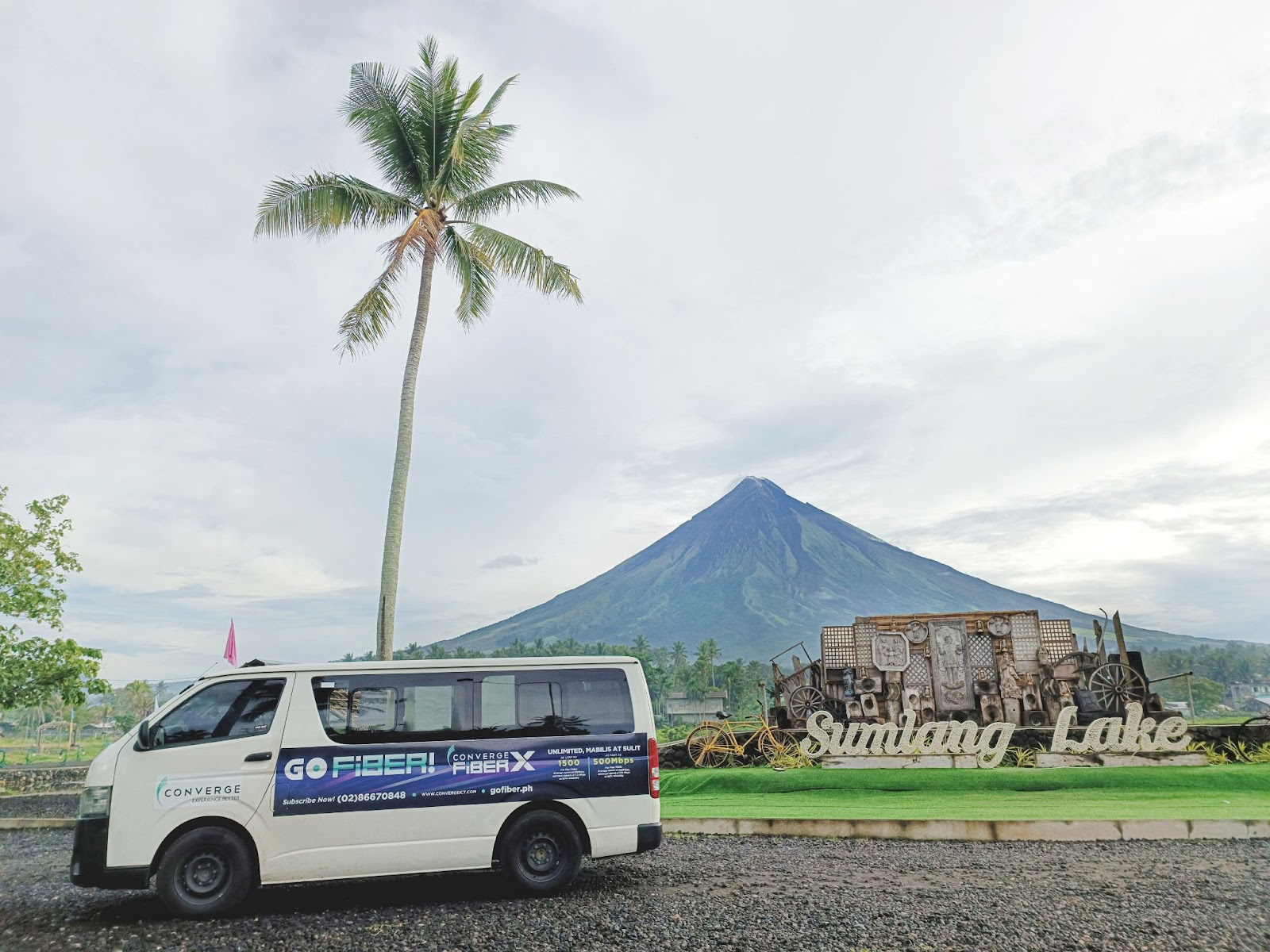 A white van parked next to a palm tree and a mountain Description automatically generated with low confidence
